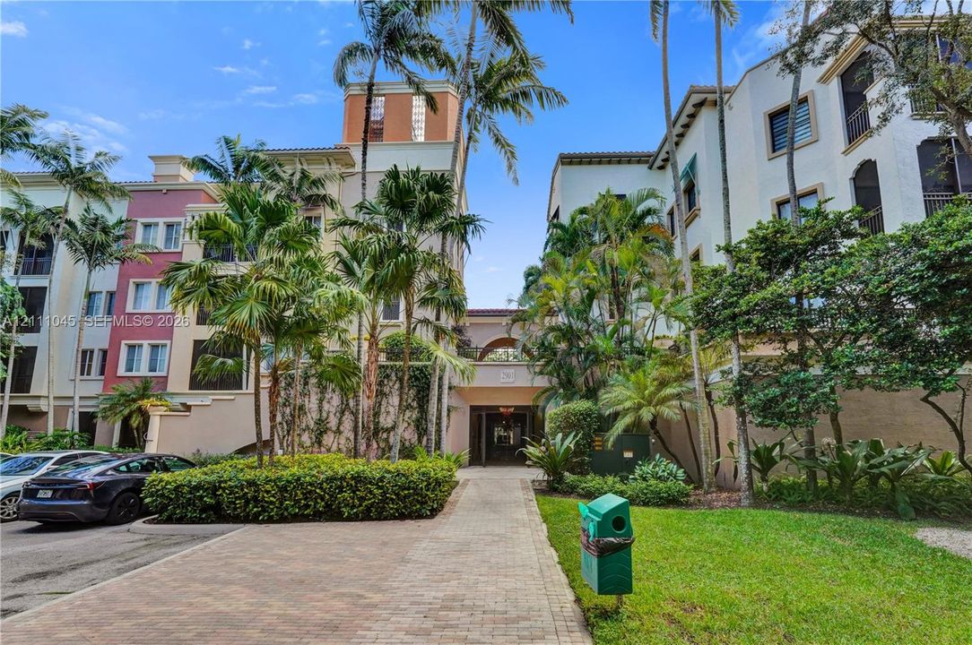 Multi-story Mediterranean-inspired exterior featuring stucco facades, arched architectural details, mature palm trees, and brick paver walkways