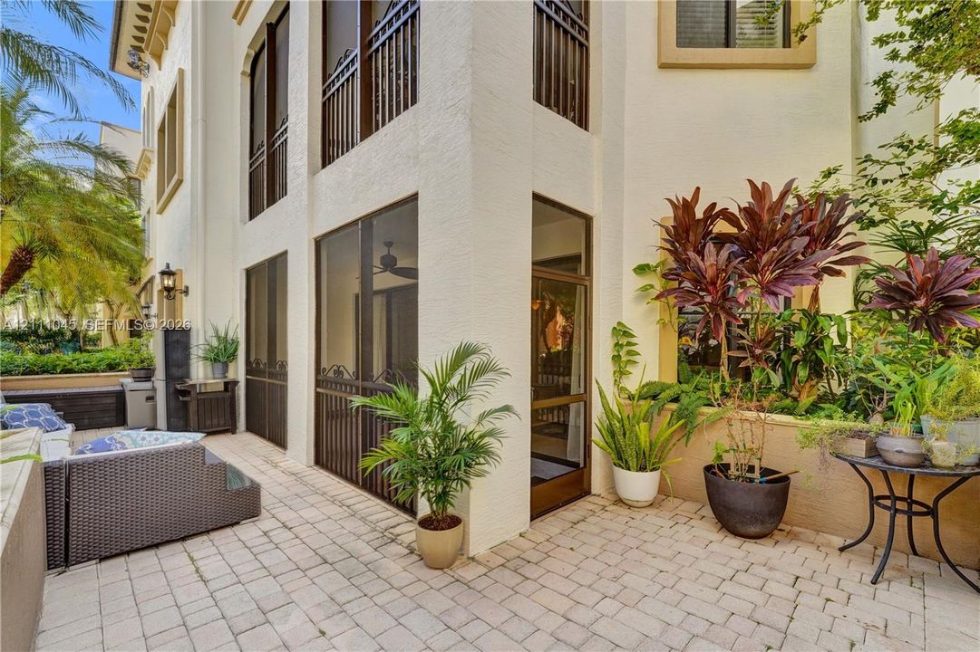 Stucco exterior featuring multiple levels, paved stone patio, screened enclosure, decorative metal railings, and attached exterior lighting
