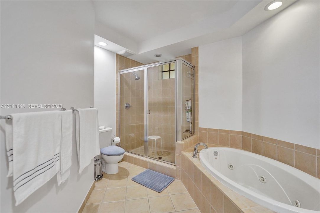 Bathroom featuring a jetted soaking tub, tiled shower enclosure with metal-framed glass door, and neutral tile flooring