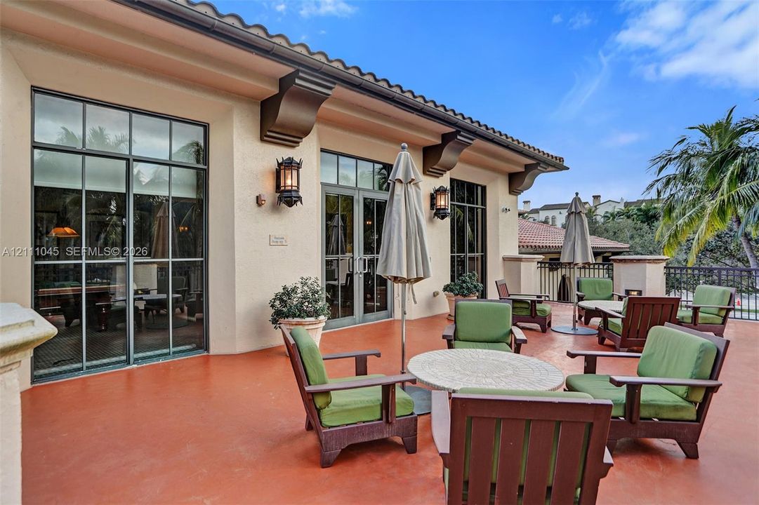 Covered outdoor terrace featuring terracotta-toned hardscaping, decorative corbels, black-framed French doors, and wall-mounted exterior lanterns