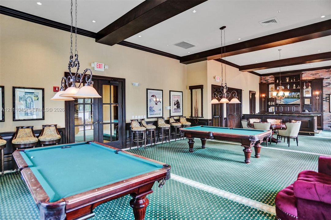Large recreation room featuring dark wood ceiling beams, decorative crown molding, a built-in wet bar with cabinetry, and recessed lighting