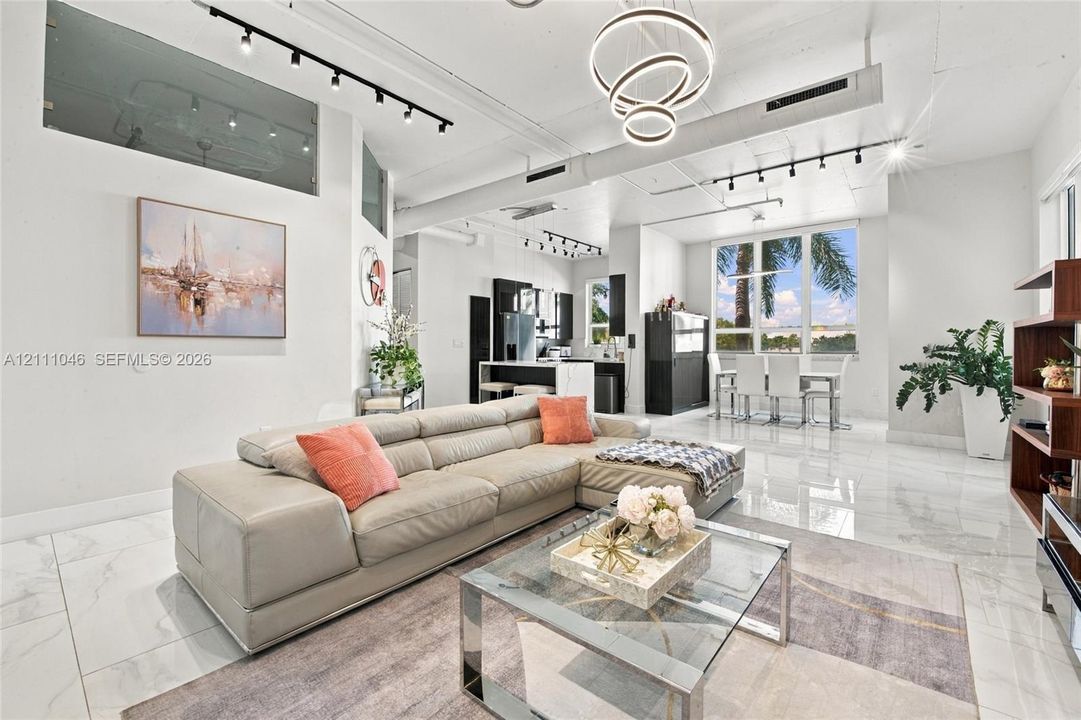 Open-concept interior featuring large-format tile flooring, exposed industrial ductwork, modern multi-ring pendant lighting, track lighting, and expansive windows