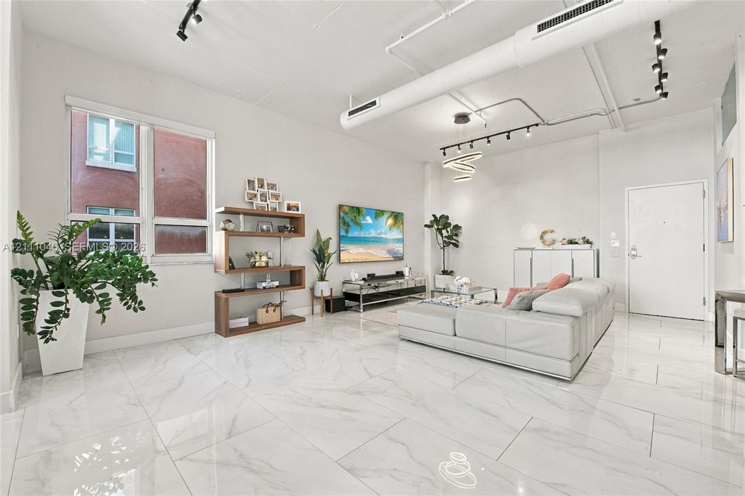 Open-concept living space featuring high ceilings with exposed industrial ductwork, large-format tile flooring, track lighting, and a modern spiral pendant fixture