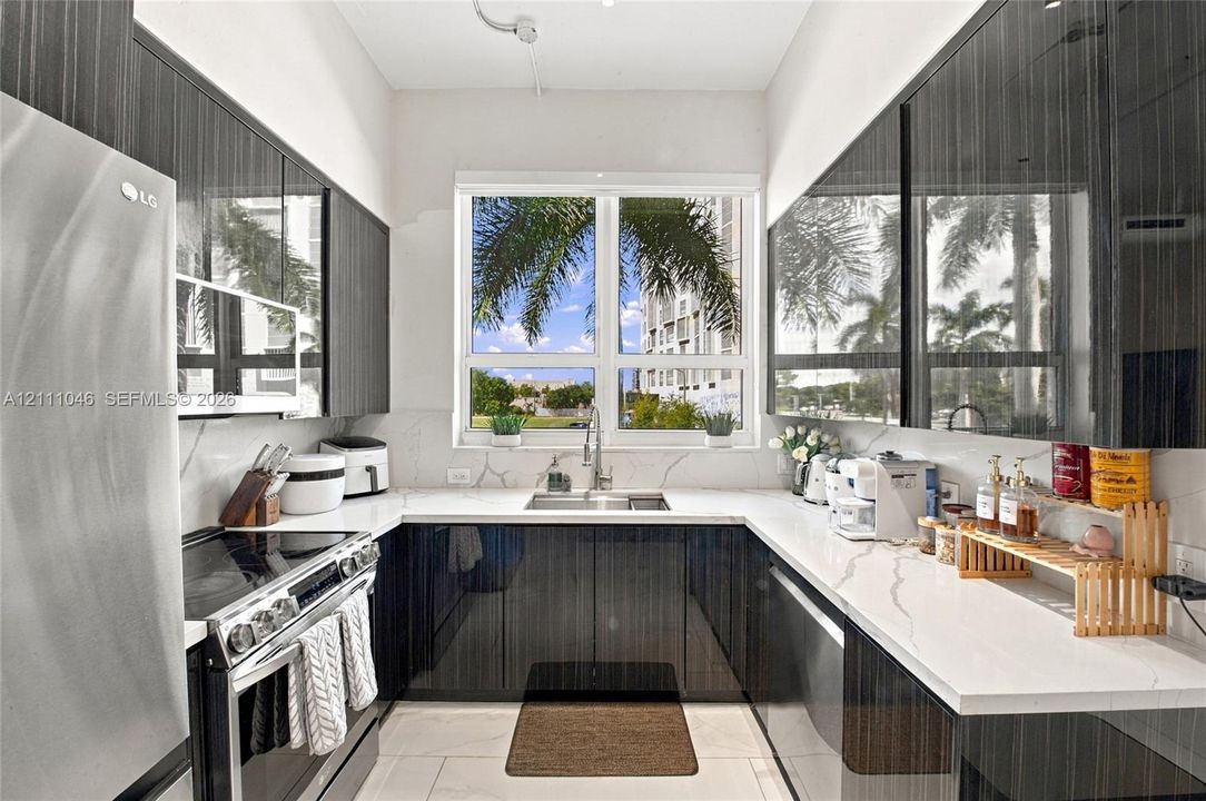 Kitchen featuring high-gloss dark cabinetry, white countertops with grey veining, a stainless steel slide-in range, a stainless steel undermount sink with a gooseneck faucet, and large-format tile flooring