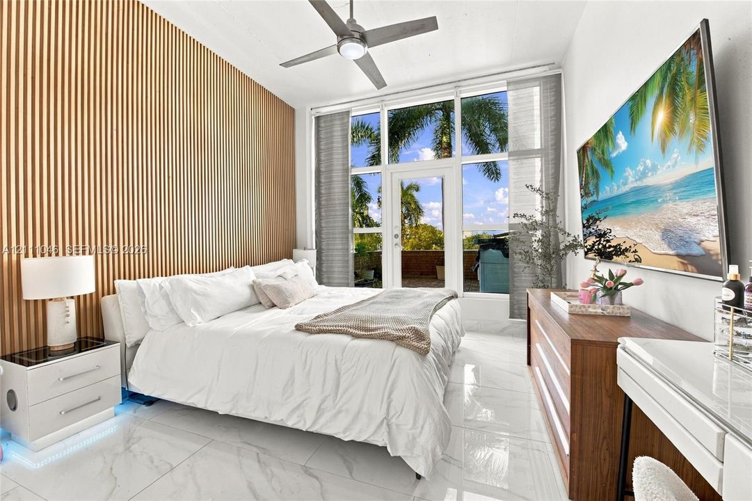 Vertical slat wood accent wall, floor-to-ceiling windows with glass exterior door, polished tile flooring, and integrated ceiling fan