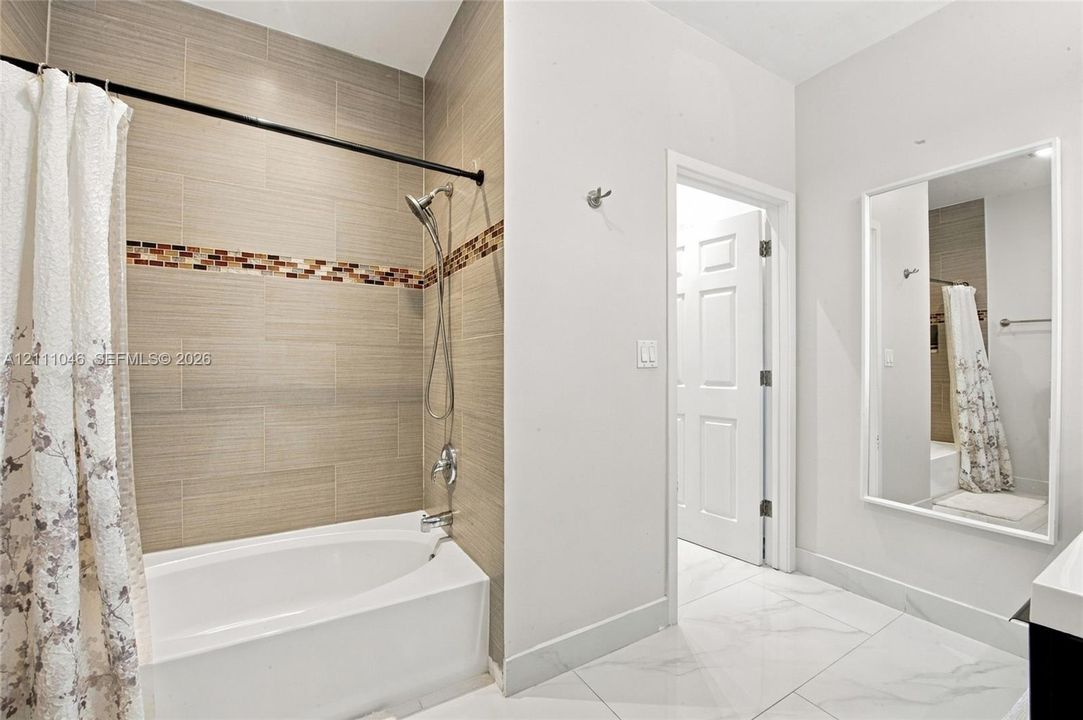 Full bathroom featuring a deep soaking tub, horizontal wall tiling with a glass mosaic accent border, handheld shower fixture, and polished large-format floor tile