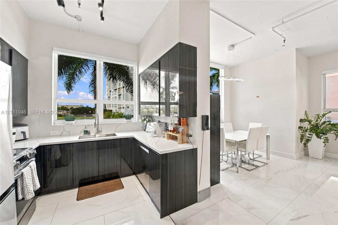 Modern kitchen featuring high-gloss dark cabinetry, stone-finish countertops, stainless steel undermount sink, large-format tile flooring, and exposed industrial-style conduit lighting