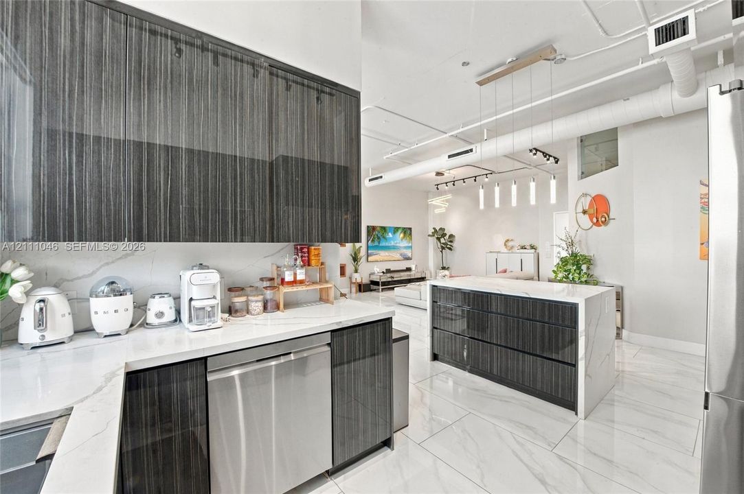 Modern kitchen featuring high-gloss charcoal cabinetry, white stone-patterned countertops, a central kitchen island, light-toned stone-patterned flooring, and industrial-style exposed ductwork