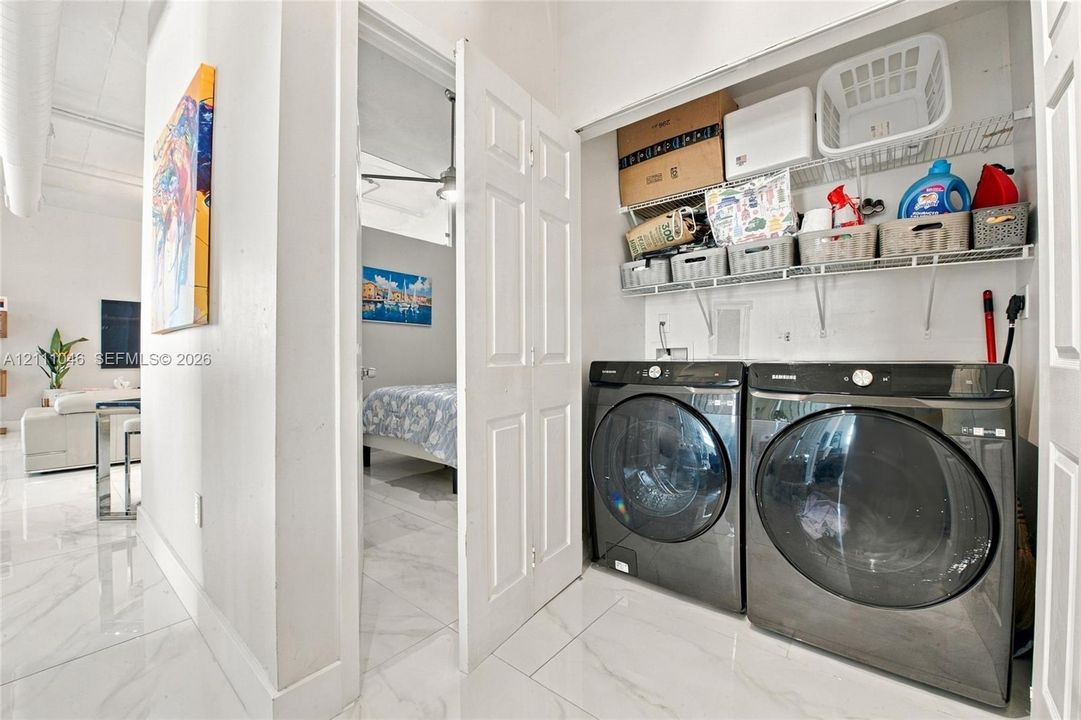 Laundry closet featuring high-capacity front-load washer and dryer with wire shelving above for storage and white tile flooring