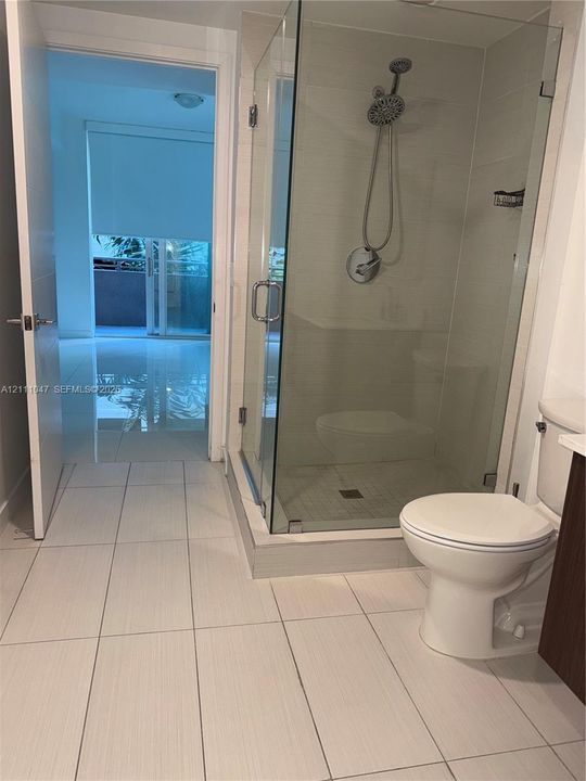Bathroom featuring a walk-in glass shower enclosure, adjustable hand-held shower head, large-format neutral floor tile, and a standard-height toilet