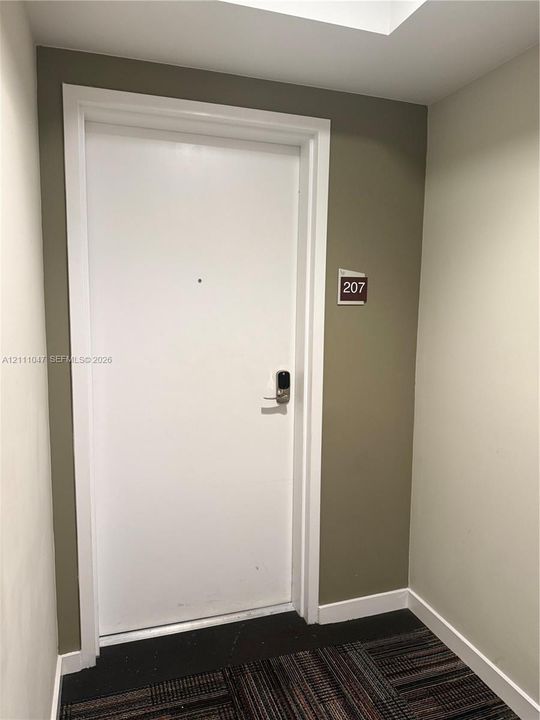 Solid white entry door featuring an electronic keyless entry system and a centrally mounted peephole