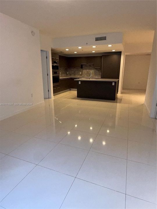 Kitchen featuring dark cabinetry, an island with countertop, built-in wall ovens, tile backsplash, and polished large-format floor tiling