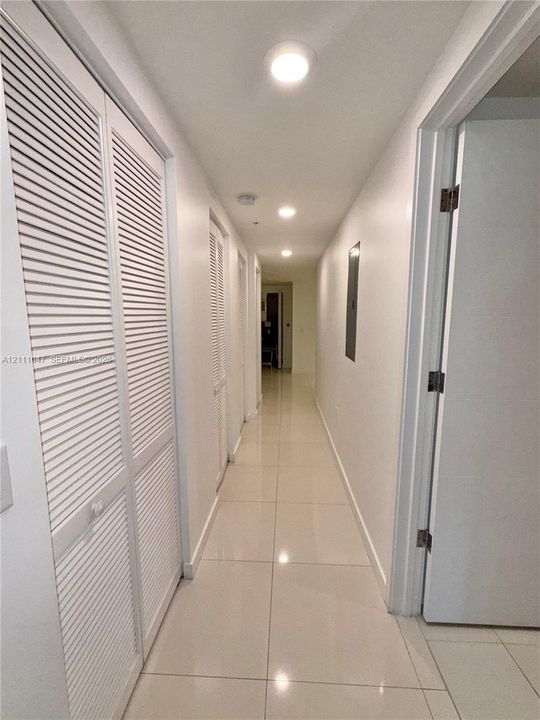 Hallway featuring large-format tile flooring, recessed ceiling lighting, and built-in closet cabinetry with louvered doors