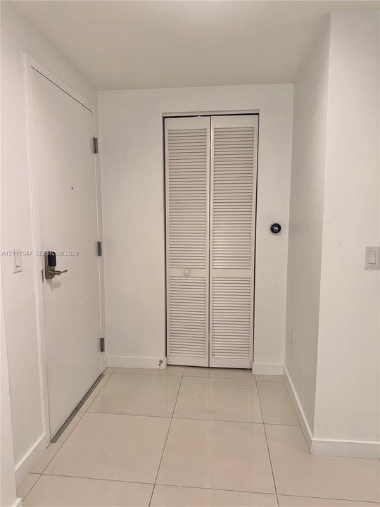 Entryway featuring large-format ceramic tile flooring, a white solid-core door with electronic keypad hardware, and white louvered bifold closet doors