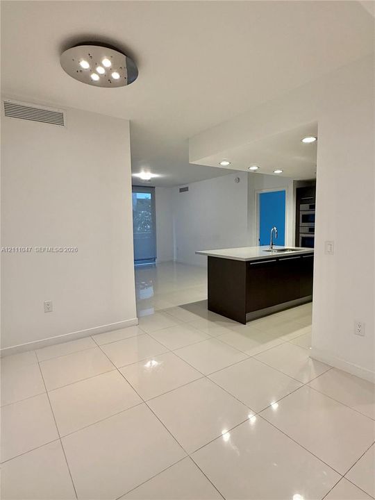 Polished porcelain tile flooring, recessed ceiling lighting, and a modern kitchen island with a stone countertop and under-mount sink