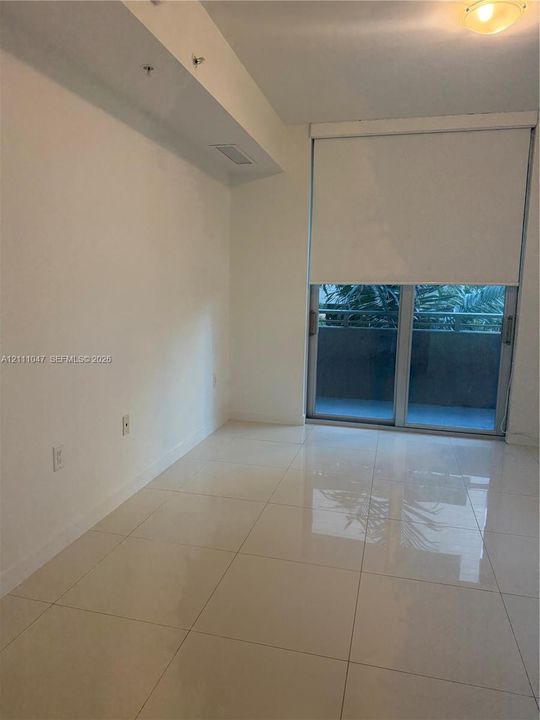 Large-format tile flooring, recessed ceiling lighting, and floor-to-ceiling glass sliding doors with an integrated roller shade