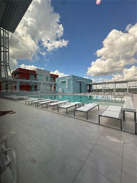 Outdoor swimming pool with a shallow sun shelf, surrounded by expansive paved decking and a metal pergola structure