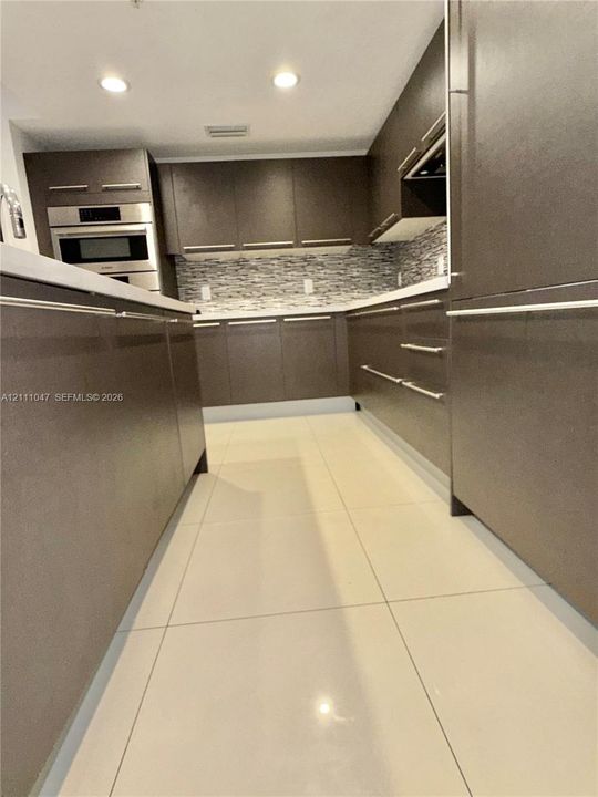 Kitchen featuring flat-panel cabinetry with horizontal pulls, light-toned tile flooring, built-in stainless steel double wall ovens, and a multicolored glass tile backsplash