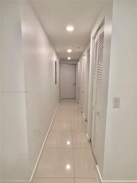 Hallway featuring large-format tile flooring, recessed ceiling lighting, and multiple white louvered closet doors