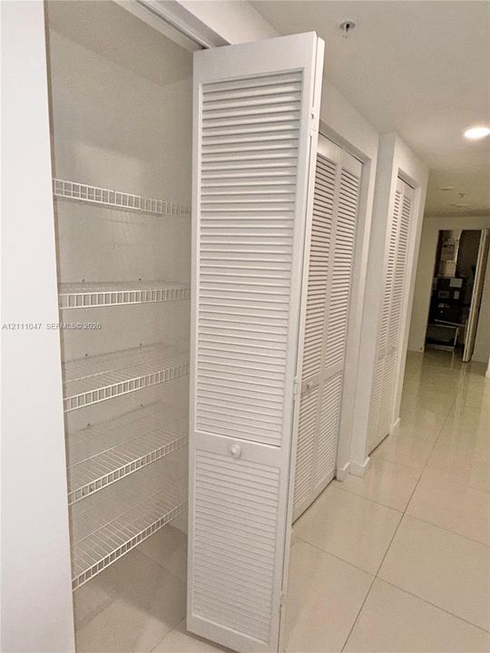 Storage area featuring white louvered doors and white wire shelving, finished with large-format neutral tile flooring