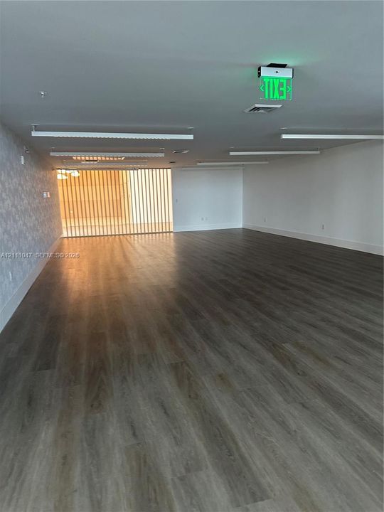 Open-concept floor plan featuring wood-finish flooring, recessed linear lighting, patterned accent wall, and vertical slat privacy screen