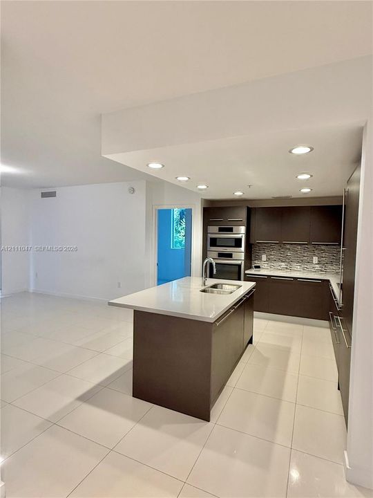 Kitchen featuring dark flat-panel cabinetry, a central island with a quartz countertop, recessed ceiling lighting, a built-in double oven, and tile flooring