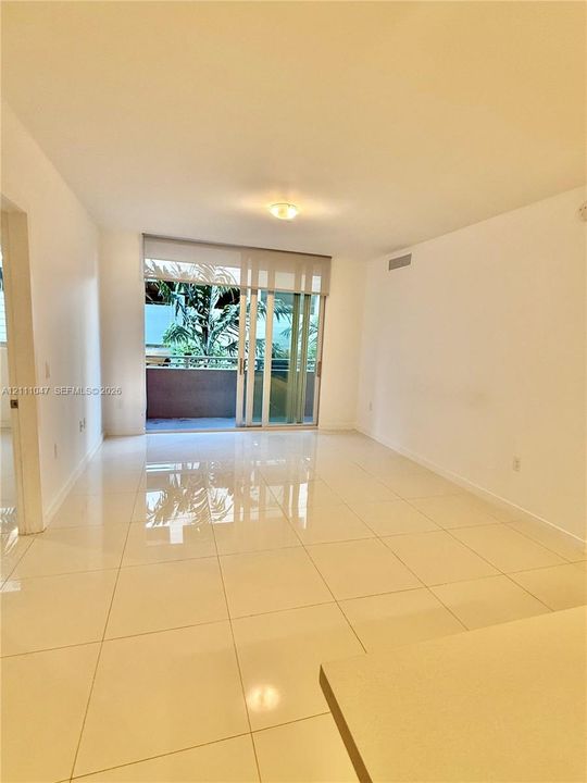 Neutral-toned interior space featuring light-colored tile flooring, flush-mount ceiling lighting, and sliding glass doors providing outdoor access to a private balcony