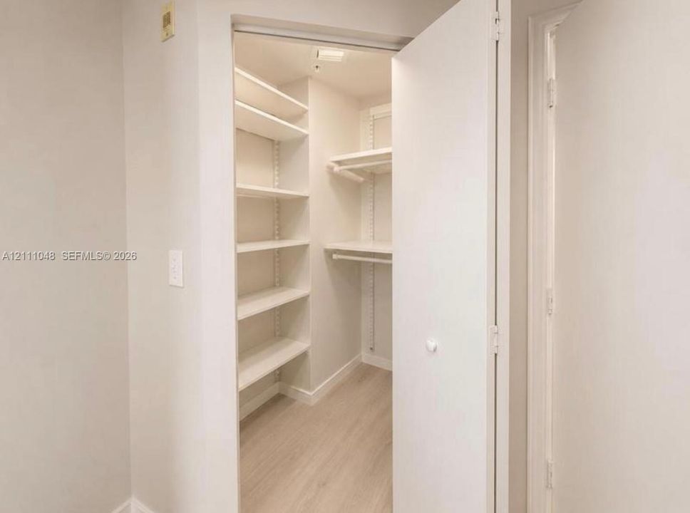 Reach-in closet featuring adjustable shelving, integrated hanging rods, and light-toned wood-finish flooring