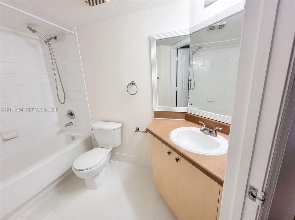 Full bathroom featuring a tub-shower combination with white wall tile, a vanity with a solid-surface countertop and integrated sink, and an expansive corner-mounted vanity mirror
