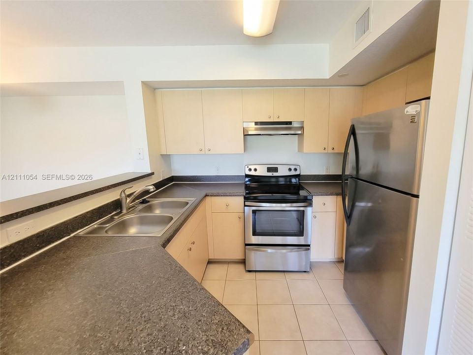 Kitchen featuring light-finish cabinetry, dark solid-surface countertops, stainless steel appliances, double-basin sink, and tile flooring