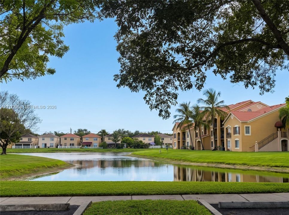 Waterfront setting with manicured lawn, mature trees, and multi-story stucco architecture