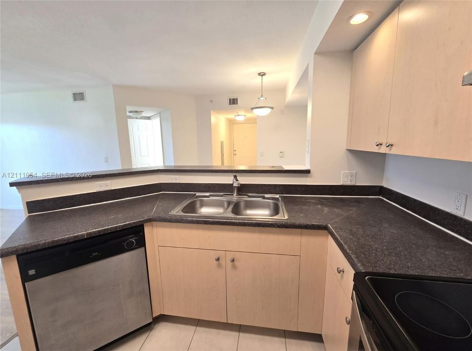 Kitchen featuring light-finish cabinetry, dark solid-surface countertops, stainless steel dual-basin sink, and recessed lighting