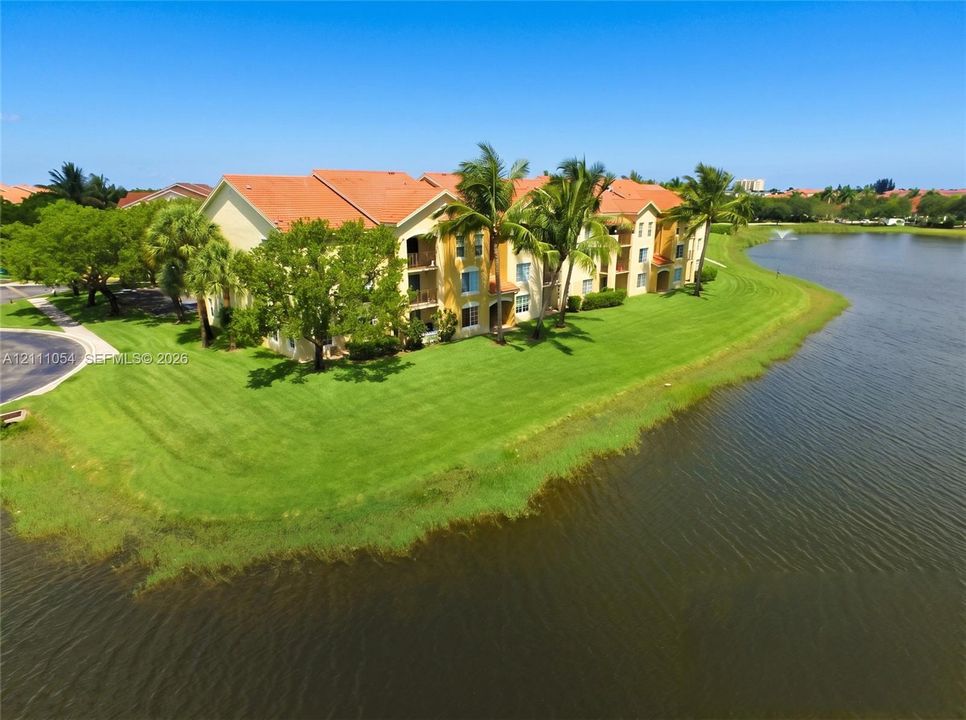 Multi-story residential building featuring a tile roof, stucco exterior, private balconies, and landscaped grounds positioned along a lakefront