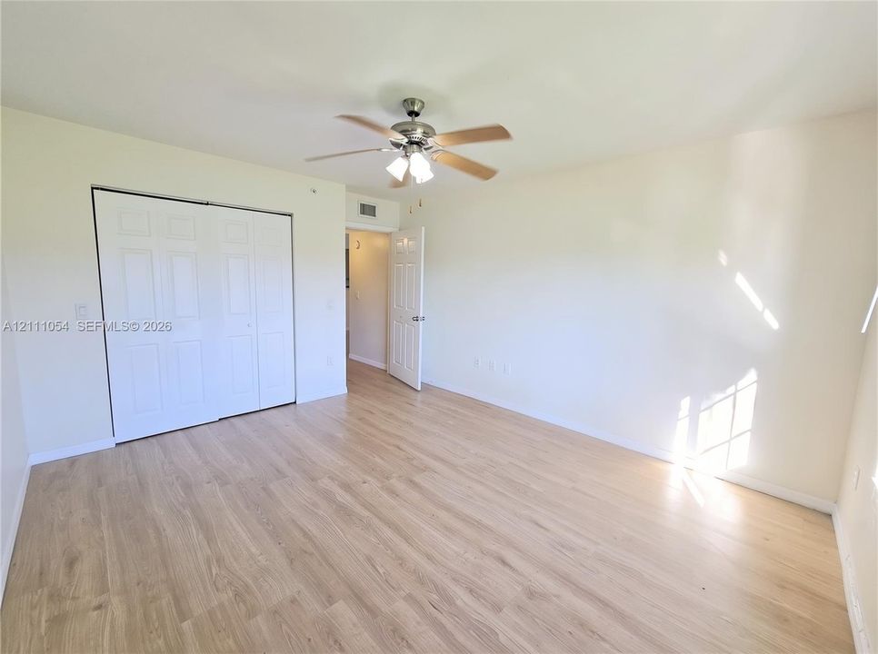 Room featuring wood-finish flooring, a ceiling fan with integrated lighting, and a six-panel sliding closet door