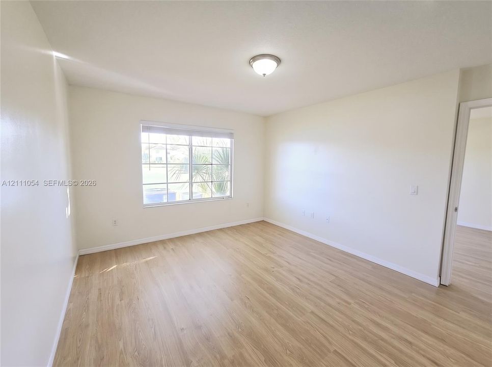 Neutral-toned interior space featuring wood-finish flooring, a grid-pattern window, and a flush-mount ceiling light fixture