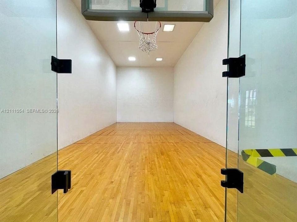 Recreational court featuring wood-finish flooring, glass enclosure, recessed ceiling lighting, and a wall-mounted basketball hoop