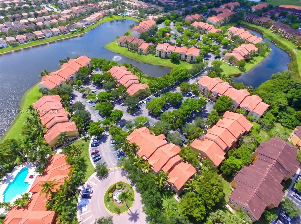 Aerial perspective of a multi-unit complex featuring terra-cotta tile roofs, waterfront positioning, an outdoor swimming pool, and mature perimeter landscaping