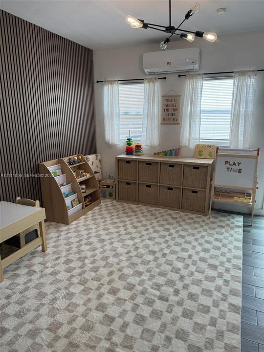 Vertical wood-slat accent wall, modern multi-arm light fixture, wall-mounted ductless HVAC unit, and neutral tile flooring