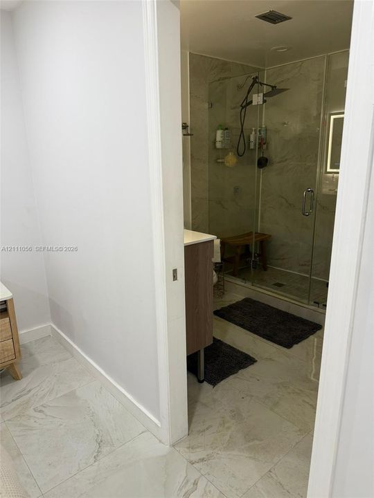 Bathroom featuring stone-finish flooring, a wood-finish vanity, and a glass-enclosed shower with a rainfall showerhead