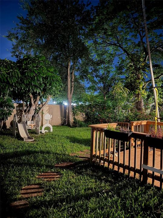 Backyard featuring a wood-decked patio with integrated railing, stone paver path, solid perimeter fencing, and mature trees