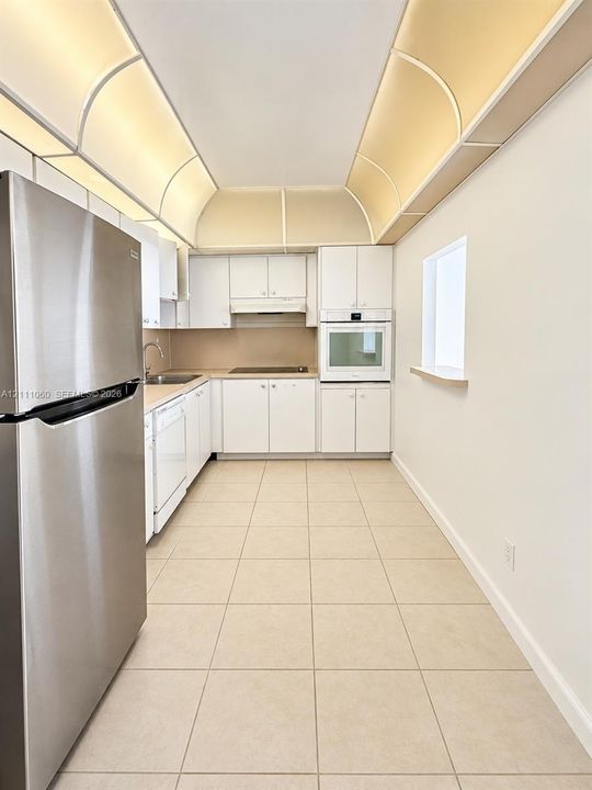 Kitchen featuring white cabinetry, stainless steel refrigerator, built-in wall oven, tile flooring, and barrel vault ceiling detail