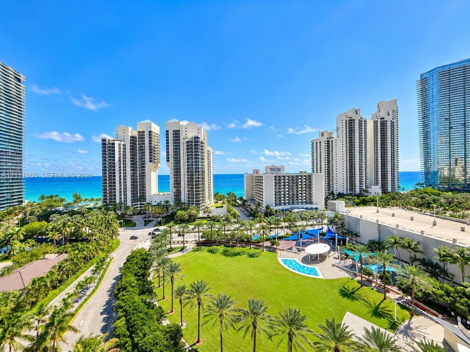 High-rise residential surroundings featuring mature palm landscaping, manicured lawn areas, a communal swimming pool, and proximity to the coastline