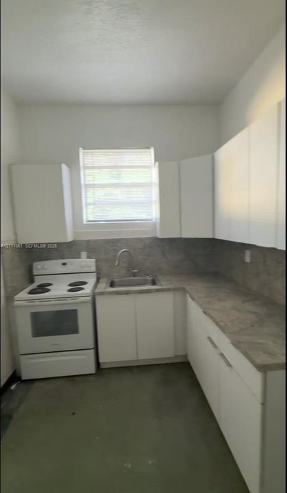 Kitchen featuring white flat-panel cabinetry, stone-patterned laminate countertops, full-height decorative backsplash, white electric range, and a single-basin stainless steel sink with an arched faucet