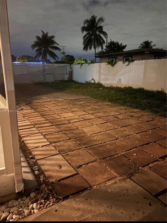 Rear patio featuring concrete pavers, enclosed by a white privacy fence with double-gate access