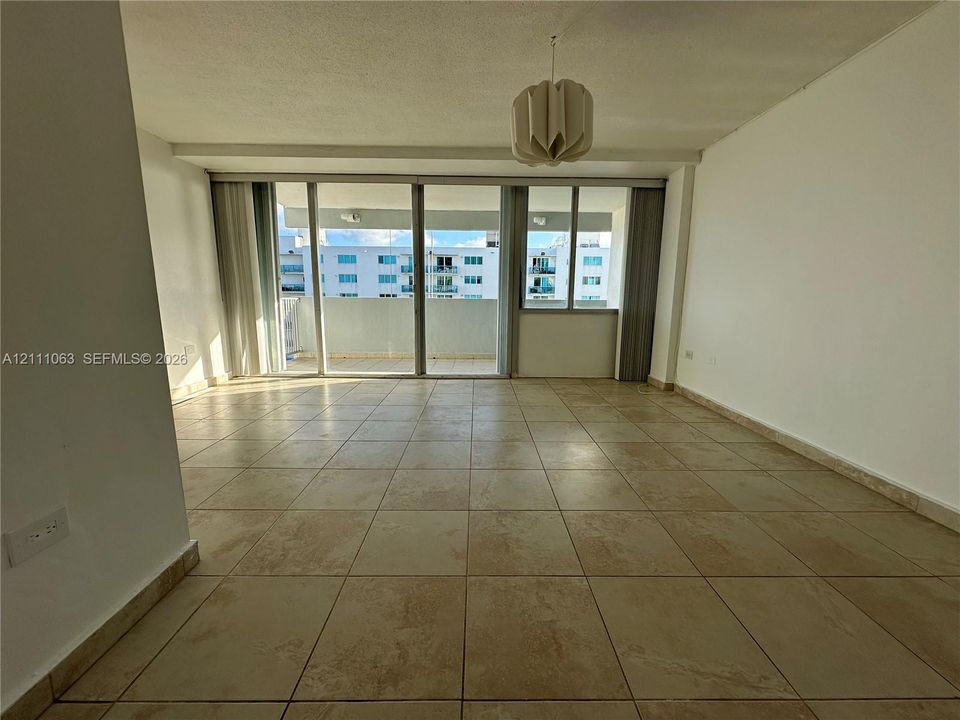 Interior space featuring large-format tile flooring, sliding glass door access to a private balcony, floor-to-ceiling windows, and a suspended multi-panel light fixture