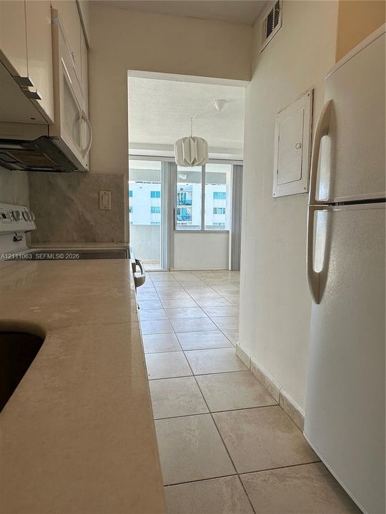 Kitchen featuring solid-surface countertops, neutral tile flooring, white cabinetry, and built-in appliances, opening to a space with floor-to-ceiling windows and a sliding glass door