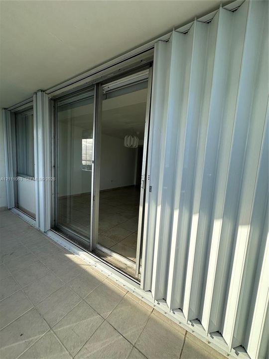 Covered balcony featuring neutral tile flooring and white accordion-style storm shutters protecting the sliding glass door entry