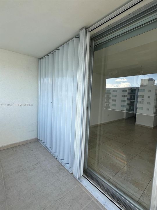Covered balcony featuring ceramic tile flooring, accordion-style metal storm shutters, and large glass sliding doors