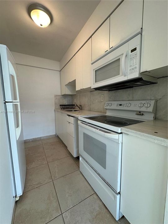 Galley kitchen featuring white cabinetry, stone-finish countertops, integrated microwave, electric range, and tile flooring