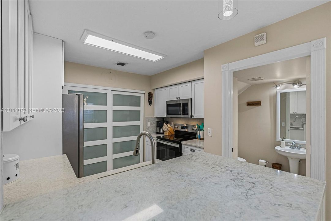 Kitchen featuring stone countertops, white cabinetry, a high-arc faucet, and frosted glass sliding doors, with a pedestal sink in the background